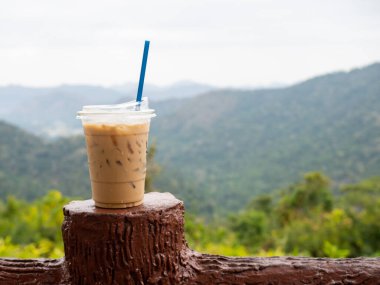 A glass of iced coffee is placed on the fence against a backdrop of mountains and sky.