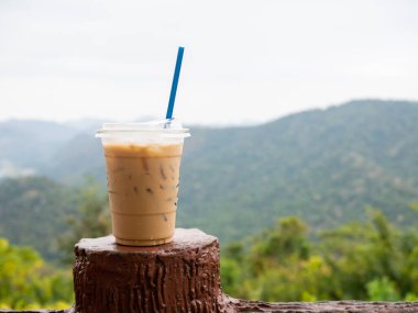 A glass of iced coffee is placed on the fence against a backdrop of mountains and sky.
