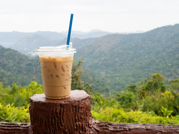 A glass of iced coffee is placed on the fence against a backdrop of mountains and sky.