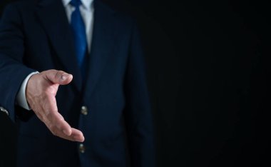 İşadamı ayakta duruyor ve karanlık arka planda el sıkışma hareketi yapıyor. İş konsepti. Boşluğu kopyala.