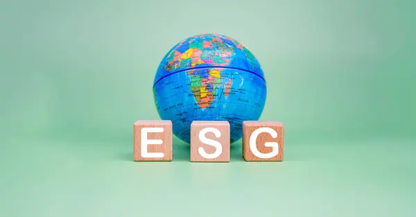 ESG concept for environment, society and governance in sustainable. business responsible environmental. Wooden blocks with ESG letters printed on them and a model of the earth on a green background.