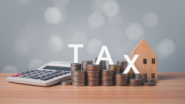 Модель деревянного дома, калькулятор и монеты выстроились на деревянном полу на белом фоне. Концепции ипотеки, займа, передачи, финансов, сбережений и инвестиций. Налог на недвижимость.