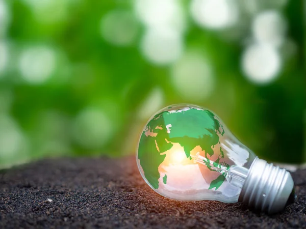 Concept of renewable energy, environmental protection, and sustainable renewable energy sources. World map on a light bulb set on soil and nature background. Green energy concept.