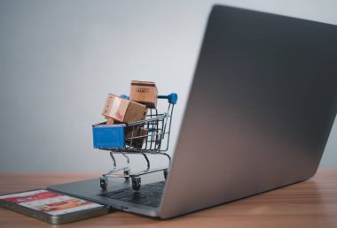 Dizüstü bilgisayara yerleştirilen alışveriş arabası ve ürün kutuları çevrimiçi alışveriş kavramı, web sitesi, e-ticaret, pazar platformu, teknoloji, ulaşım, lojistik ve çevrimiçi ödeme kavramını temsil etmektedir..