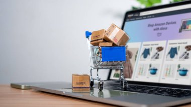 Dizüstü bilgisayara yerleştirilen alışveriş arabası ve ürün kutuları çevrimiçi alışveriş kavramı, web sitesi, e-ticaret, pazar platformu, teknoloji, ulaşım, lojistik ve çevrimiçi ödeme kavramını temsil etmektedir..