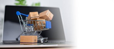 Dizüstü bilgisayara yerleştirilen alışveriş arabası ve ürün kutuları çevrimiçi alışveriş kavramı, web sitesi, e-ticaret, pazar platformu, teknoloji, ulaşım, lojistik ve çevrimiçi ödeme kavramını temsil etmektedir..