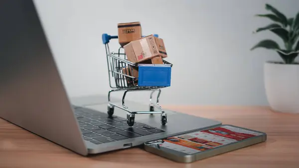 Dizüstü bilgisayara yerleştirilen alışveriş arabası ve ürün kutuları çevrimiçi alışveriş kavramı, web sitesi, e-ticaret, pazar platformu, teknoloji, ulaşım, lojistik ve çevrimiçi ödeme kavramını temsil etmektedir..
