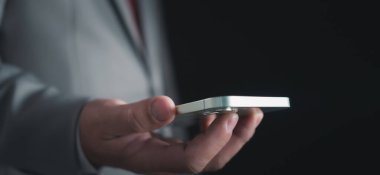 Karanlık arka planda akıllı telefonu tutan iş adamının yakın plan çekimi iş iletişimi kavramlarını temsil ediyor.