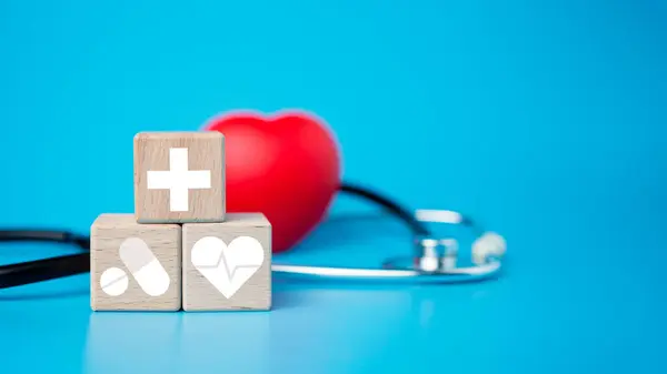 The concept of health insurance and medical welfare. Block wooden and red heart with plus icon. Health insurance and access to health care.