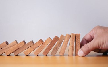 İşadamı eli masaya düşen engelleri durdurdu, iş çözümü, strateji ve başarılı müdahale için domino etkisi kavramını durdurdu.