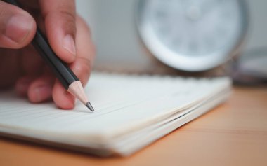 Ahşap masa yüzeyinde insan eli kalemle notlar yazıyor..
