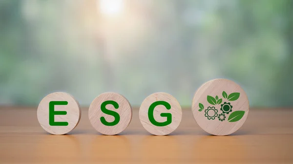 A circular wooden board is placed on a wooden floor with letters printed showing ESG concepts for sustainable environment, society and governance. Businesses are environmentally responsible.