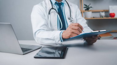 Çalışma masasında oturan erkek doktor çalışma planlarını kontrol ediyor ve hastane ofisinde belge raporları yazıyor, sağlık çalışanı ve doktor servisi, modern ofiste dijital dizüstü bilgisayar, tıbbi teknoloji kavramı.