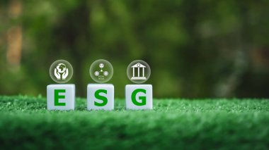 Üzerinde ESG harfleri yazılı üç beyaz küpten oluşan bir grup, küpleri yeşil çimenli bir alana yerleştiriliyor, uyum ve denge hissi yaratıyor, ESG harfleri daha küçük harflerle çevrili..