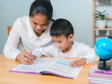 Evde bireysel ders sırasında küçük bir ilkokul çocuğuna ev ödevlerinde yardım eden öğretmen ya da anne çocuğun yazma ve yazmayı öğrenmesine yardım eden öğretmen, evde eğitim konsepti. 