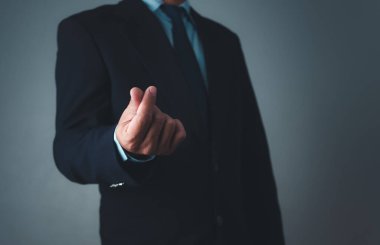 Takım elbiseli bir işadamı gri arka planda küçük bir kalp hareketi yapıyor.