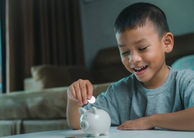 Asyalı çocuk kumbarada para biriktiriyor, bir şeyler düşünmeyi öğreniyor, çocuk gelecek eğitim için para biriktiriyor. Para, finans, sigorta ve insan konsepti.