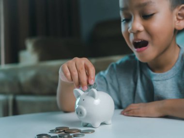 Asyalı çocuk kumbarada para biriktiriyor, bir şeyler düşünmeyi öğreniyor, çocuk gelecek eğitim için para biriktiriyor. Para, finans, sigorta ve insan konsepti.