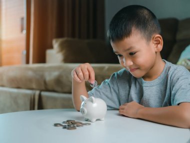 Asyalı çocuk kumbarada para biriktiriyor, bir şeyler düşünmeyi öğreniyor, çocuk gelecek eğitim için para biriktiriyor. Para, finans, sigorta ve insan konsepti.