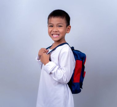 Beyaz giyinmiş, beyaz çantalı, beyaz arka planda duran Asyalı sevimli çocuk mutlu ve mutlu görünüyor..