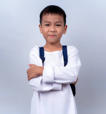 Beyaz giyinmiş, beyaz çantalı, beyaz arka planda duran Asyalı sevimli çocuk mutlu ve mutlu görünüyor..