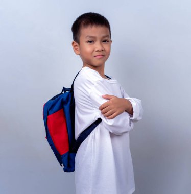 Beyaz giyinmiş, beyaz çantalı, beyaz arka planda duran Asyalı sevimli çocuk mutlu ve mutlu görünüyor..