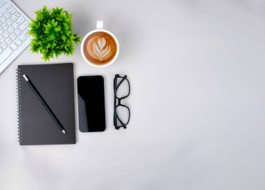 Boş ekran akıllı telefonu, klavyesi, kahve fincanı, defteri, gözlüğü olan modern çalışma alanının üst görüntüsü. Klavye ve aksesuarlarla ilgili ofis durumu beyaza izole edildi. Uzayı kopyala, düzleştir.