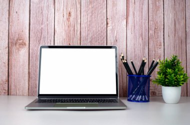 Beyaz masadaki boş ekranlı dizüstü bilgisayar ve ahşap arka planda ofis malzemeleri. Metnini kopyalamak için boşluk. Çalışma alanı ve kopyalama alanı. Ofis malzemeleriyle dolu masa..