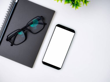 Boş ekran akıllı telefonu, kahve fincanı, defter, kalem, gözlük ile modern çalışma alanının üst görüntüsü. Klavye ve aksesuarlarla ilgili ofis durumu beyaza izole edildi. Uzayı kopyala, düzleştir.