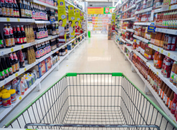 Shopping cart in supermarket, Trolley in department store Abstract blurred of colorful shelves, Empty red shopping cart view with warm light.