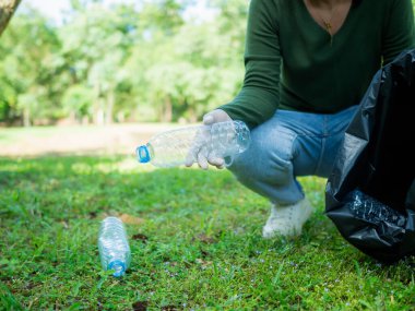 Gönüllü bir kadın parktaki bir çevre temizleme etkinliğine katılıyor. Eldiven takan ve büyük siyah çantalar tutan bir kadın. Parkta çöp ve plastik şişe toplayan bir kadın..