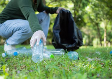 Gönüllü bir kadın parktaki bir çevre temizleme etkinliğine katılıyor. Eldiven takan ve büyük siyah çantalar tutan bir kadın. Parkta çöp ve plastik şişe toplayan bir kadın..