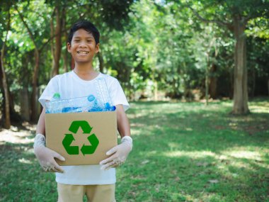Çocuk, geri dönüşüm için mukavva kutular tutuyor ve açık havada plastik şişeli bir geri dönüşüm kutusu tutuyor, çevre kirliliğini azaltma ve geri dönüşüm konsepti, plastik içermeyen, ıvır zıvır plastik ambalaj.