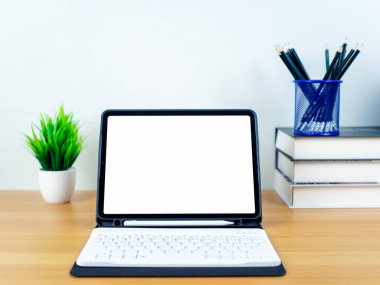 Tahta masada boş ekranlı tablet. Ofis malzemeleri, kitaplar, ev bitkileri, ahşap masa ve beyaz duvar. Metninizi, çalışma alanınızı ve kopyalama alanınızı kopyalamak için boşluk, ofis malzemelerinizi içeren masa.