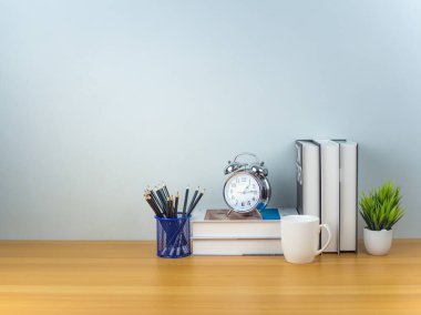 Çalışma alanı, kahve fincanı, kalem, kitap, alarm saati ve yeşil ev bitkisi ile beyaz masa modeli, ürün görüntüleme montajı için kopyalama alanı olan kopya masası, malzeme ile minimalist çalışma alanı.