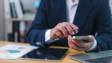 Ofis masasında dijital iletişim ya da finansal analiz için akıllı telefon kullanan işadamı, mobil verimliliği, iş dünyasındaki teknolojiyi ve çevrimiçi veri yönetimini temsil ediyor.