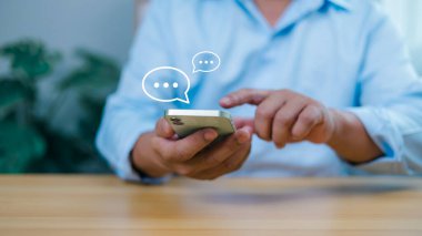 Sohbet baloncuklu akıllı telefon tutan kişi, çevrimiçi iletişimi, sosyal medyayı, mesajlaşmayı ve dijital bağlantıyı temsil ediyor. Müşteri hizmetleri, ağ kurulumu ve sanal etkileşimler için ideal.