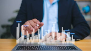 İş adamı, bir dizüstü bilgisayarın üstündeki holografik bar tablosunu, finansal büyümeyi, pazar analizini ve verilerle ilgili kararları analiz eder. İş başarısı, yatırım sezgileri ve finans teknolojisi görselleri.