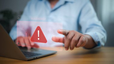 Siber güvenlik tehditleri, veri ihlalleri, sistem savunmasızlıkları ve dijital risk yönetimi. Holografik UYARI ile etkileşimde olan kişi! dizüstü bilgisayarın üzerinde kırmızı üçgen ünlem işareti.
