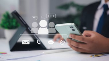 İş adamı ofis ortamında e-posta, telefon, sohbet ve grup simgeleri, dijital iletişim ve çevrimiçi müşteri destek kavramını kullanan akıllı telefon kullanıyor.