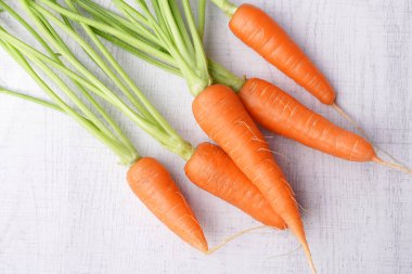 Beyaz ahşap arka planda yaprakları olan organik havuçlar..