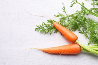 Beyaz ahşap arka planda yaprakları olan organik havuçlar..