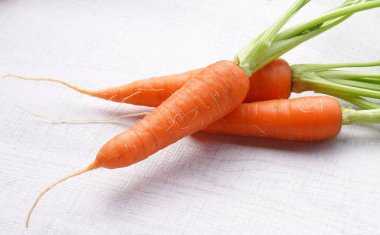 Beyaz ahşap arka planda yaprakları olan organik havuçlar..