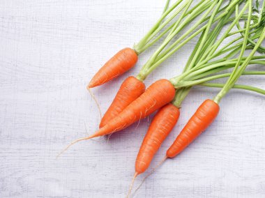 Beyaz ahşap arka planda yaprakları olan organik havuçlar..