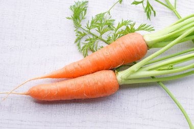 Beyaz ahşap arka planda yaprakları olan organik havuçlar..