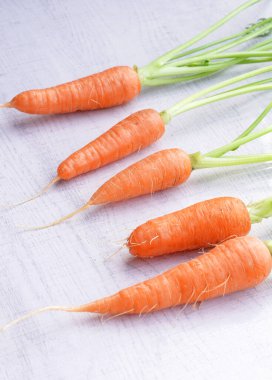 Beyaz ahşap arka planda yaprakları olan organik havuçlar..