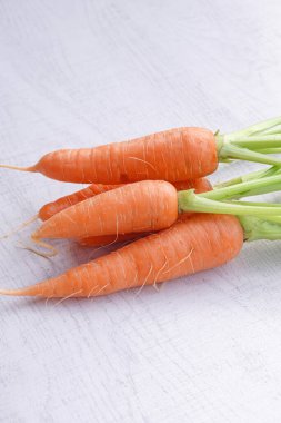 Beyaz ahşap arka planda yaprakları olan organik havuçlar..