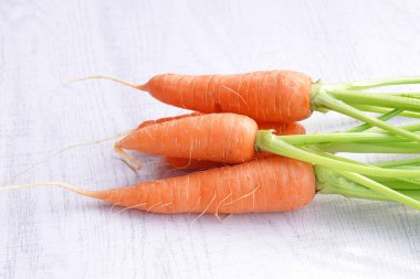 Beyaz ahşap arka planda yaprakları olan organik havuçlar..