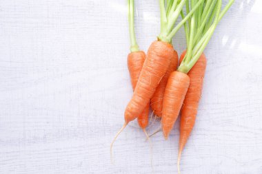 Beyaz ahşap arka planda yaprakları olan organik havuçlar..