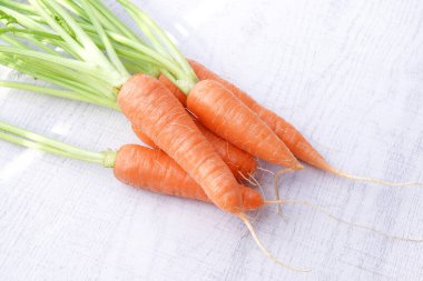 Beyaz ahşap arka planda yaprakları olan organik havuçlar..